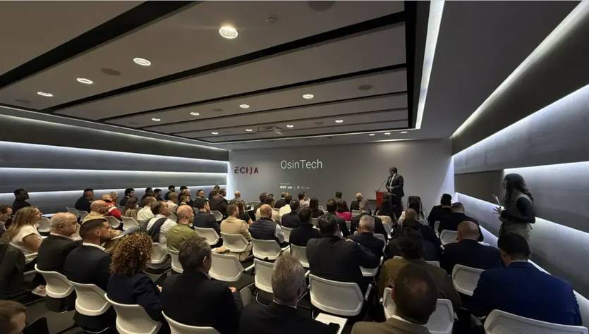 Una conferencia en un salón moderno con una gran audiencia prestando atención al ponente en el escenario.