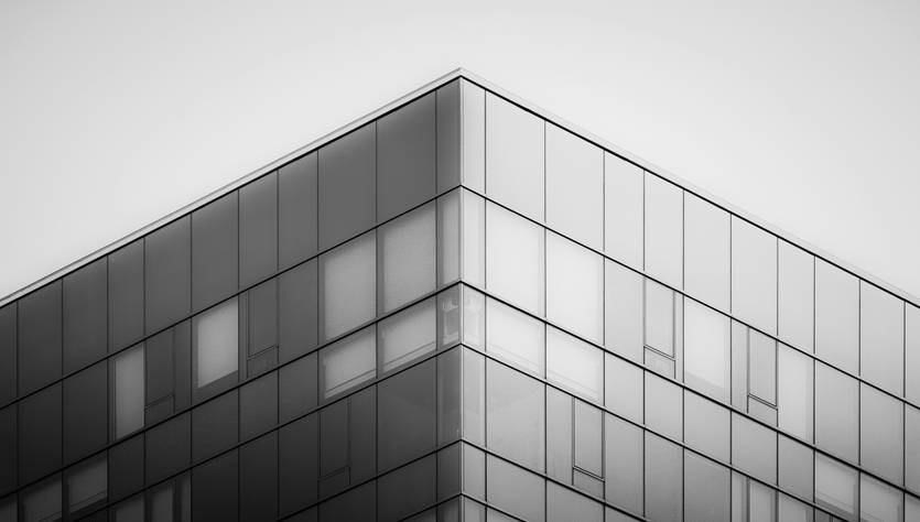 La imagen muestra la esquina superior de un edificio moderno con un diseño de cristal en blanco y negro.