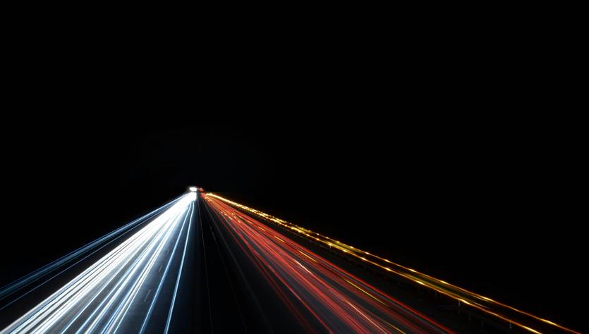 Una carretera iluminada con luces de vehículos en movimiento contra un fondo oscuro.