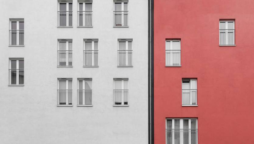 Una fachada urbana dividida entre colores blanco y rojo con ventanas en ambas secciones.