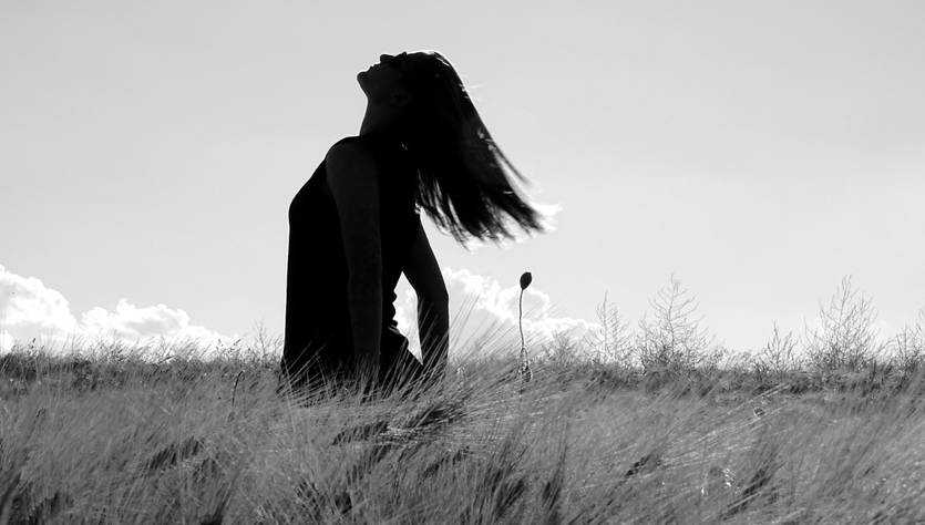 Una mujer de pie en un campo, con el cabello al viento y mirando hacia arriba.