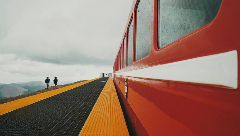Una vista de un tren rojo estacionado junto a una plataforma amarilla con dos personas caminando en la distancia.