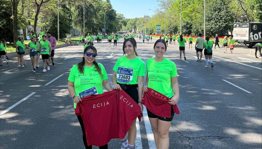 Tres personas posando con camisetas verdes en una carrera con otros participantes al fondo.