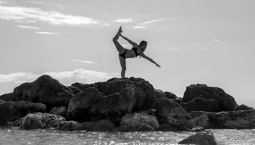 Una mujer realiza una postura de yoga sobre unas rocas frente al mar.