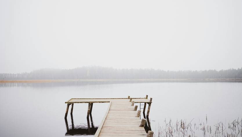 Un muelle de madera se extiende sobre un lago en un día brumoso.