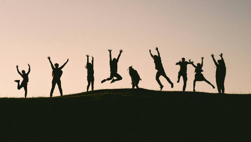 Un grupo de personas en silueta saltando y levantando las manos al aire en un atardecer.