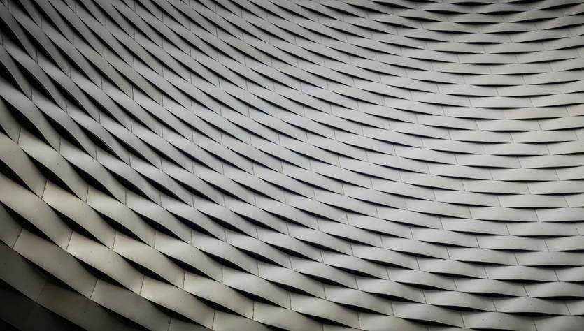 Una superficie arquitectónica con un diseño ondulado y repetitivo en tonos grisáceos.