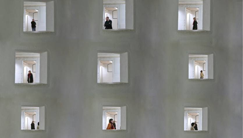 La imagen muestra un edificio con varios huecos que tienen personas de pie dentro de ellos.