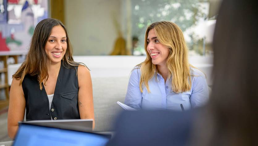 Dos mujeres sonriendo durante una conversación en un ambiente de trabajo.