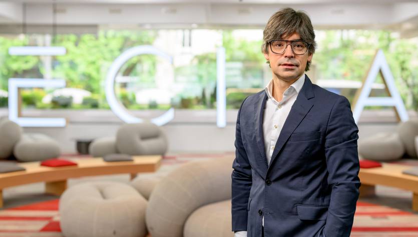 Un hombre de pie en un ambiente moderno y acogedor con mobiliario suave y un fondo luminoso.