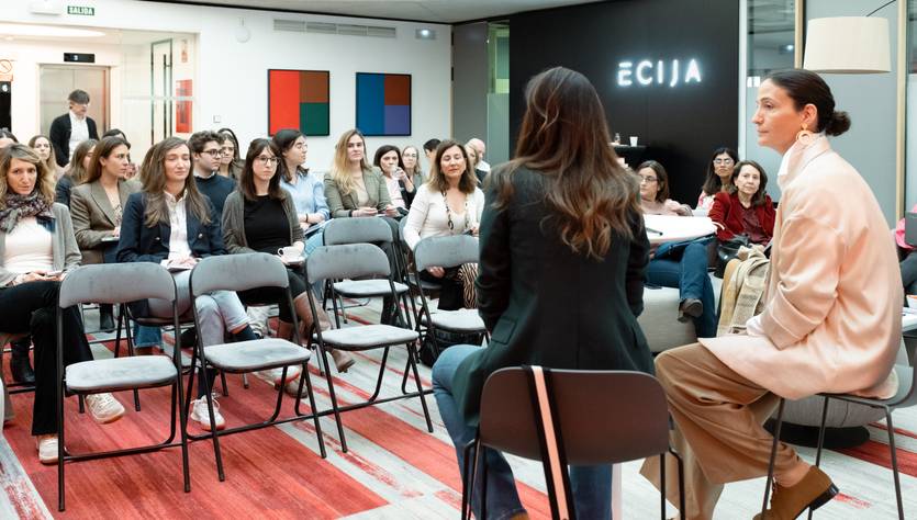 Una conferencia con un público mayoritariamente femenino escuchando a dos ponentes en un espacio moderno.