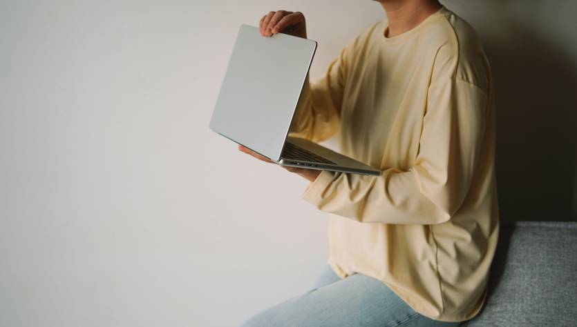 Una persona sostiene una computadora portátil mientras se sienta en un sofá.