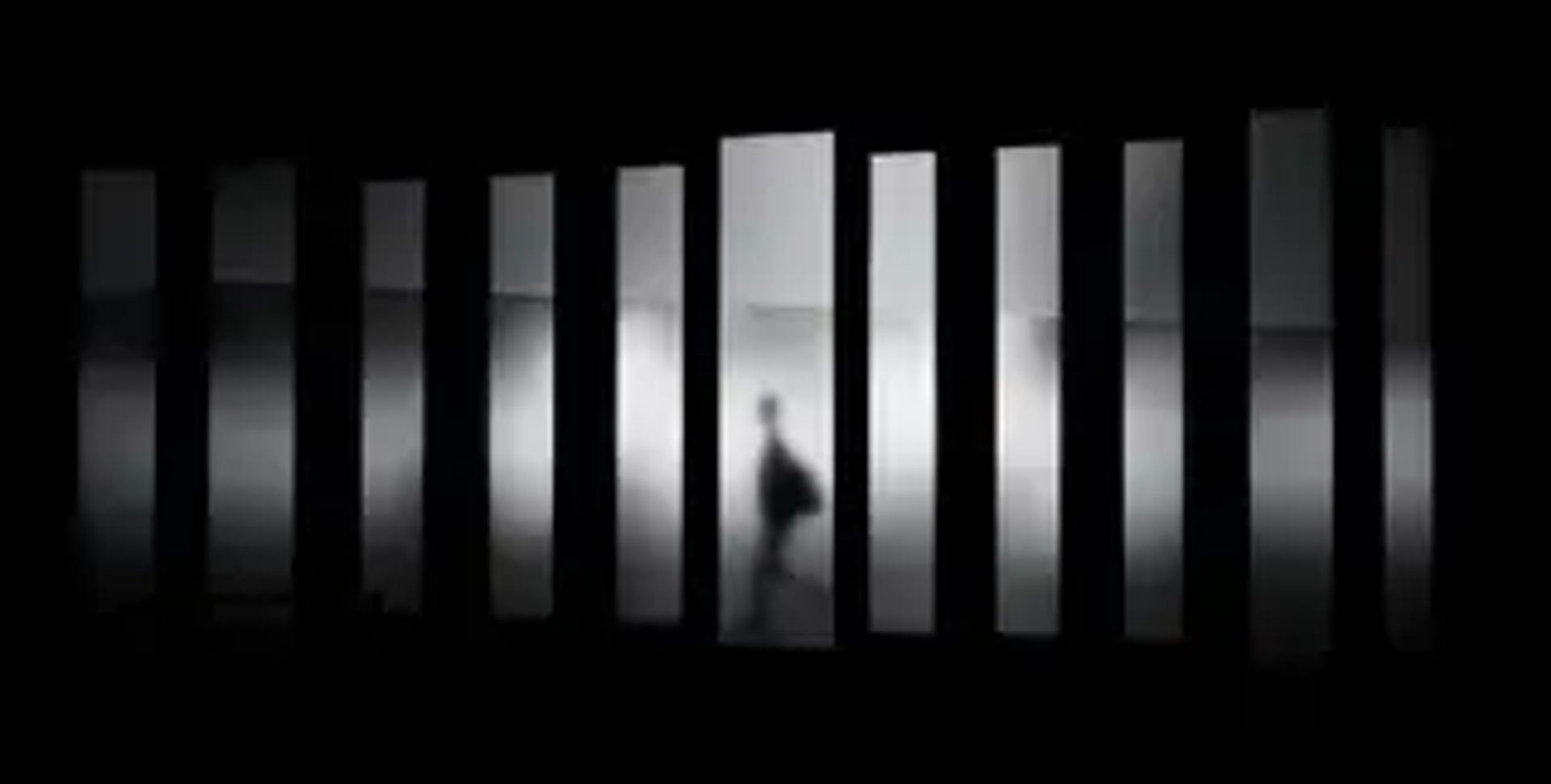 Una silueta camina entre columnas iluminadas sobre un fondo oscuro.