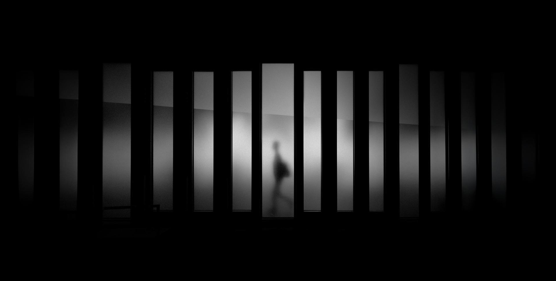 Una figura humana camina detrás de unas columnas en un ambiente oscuro y minimalista.