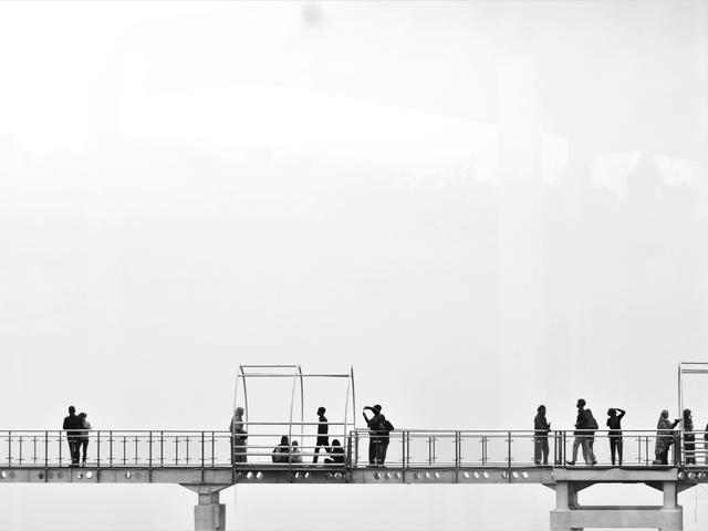 Un puente con varias personas en movimiento y estructuras para sentarse bajo una atmósfera brumosa.