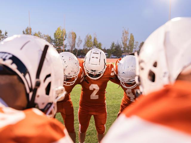Un grupo de jugadores de fútbol americano se reúne en círculo, preparándose para el juego.