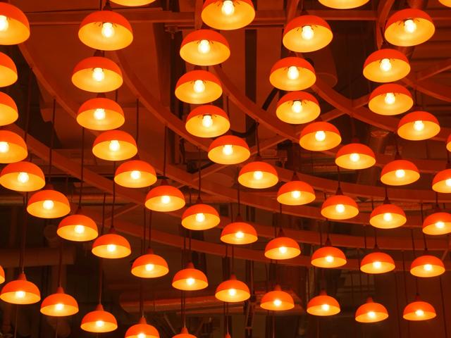 La imagen muestra una serie de lámparas colgantes de color naranja iluminadas.