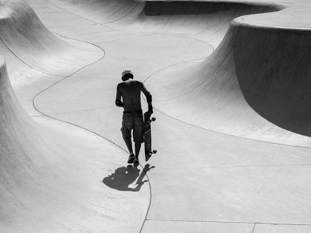Un skater camina por un parque de patinaje vacío y curvado.