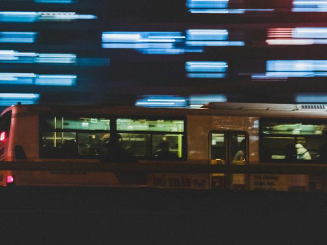 Un autobús en movimiento, capturado con un efecto de desenfoque, mientras las luces de la ciudad se iluminan de fondo.
