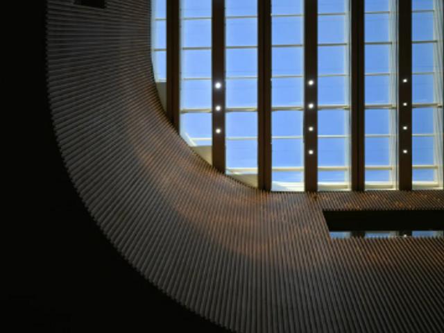 La imagen muestra un diseño arquitectónico con una curva prominente y un cielo visible a través de grandes ventanales.