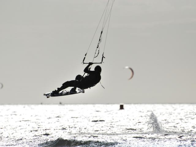 Una persona practicando kitesurf en el mar con varias cometas al fondo.
