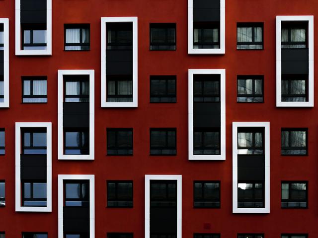 La imagen muestra una fachada moderna de un edificio con paneles de color rojo y ventanas enmarcadas en blanco.