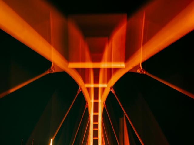 La imagen muestra un puente iluminado con luces de tono naranja contra un fondo oscuro.