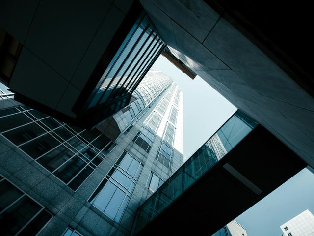 La imagen muestra un edificio alto visto desde abajo, con una perspectiva que resalta su arquitectura moderna y las fachadas de vidrio.