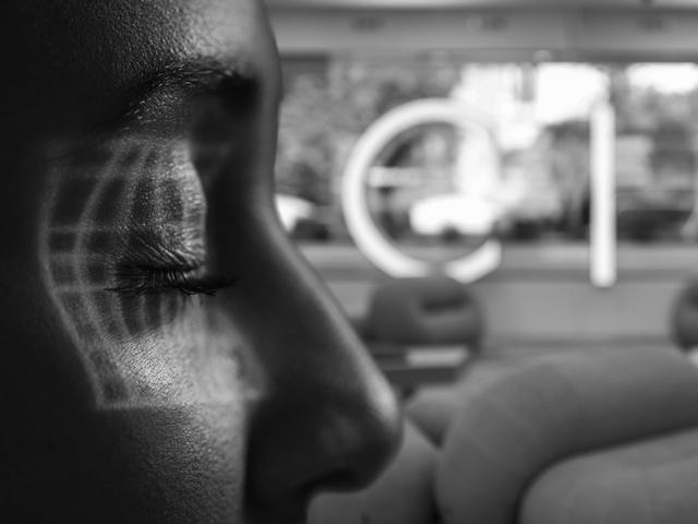 Una mujer de perfil con una proyección en su rostro y un fondo desenfocado que muestra un ambiente moderno.