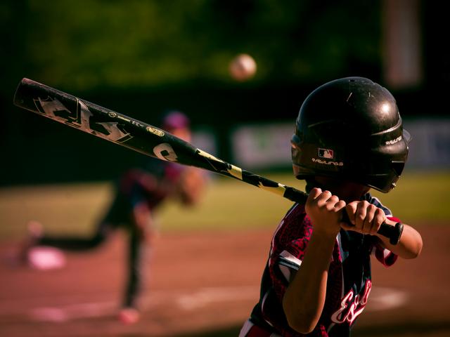 Un joven jugador de béisbol se prepara para batear una pelota lanzada por su compañero.