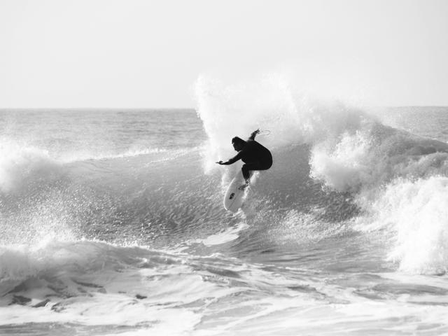 Un surfista ejecutando una maniobra sobre una ola en blanco y negro.