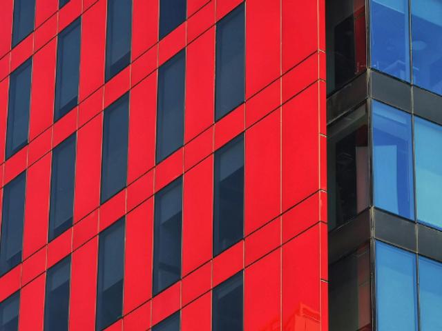 La imagen muestra un edificio moderno con una fachada de colores rojo y azul.