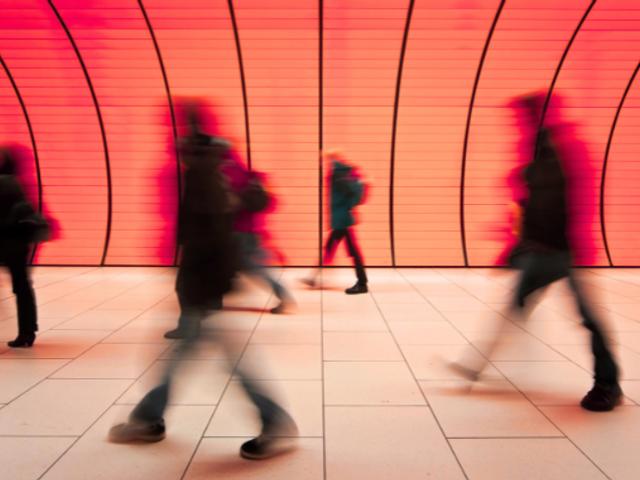 Un grupo de personas camina rápidamente frente a una pared iluminada en tonos rojos.