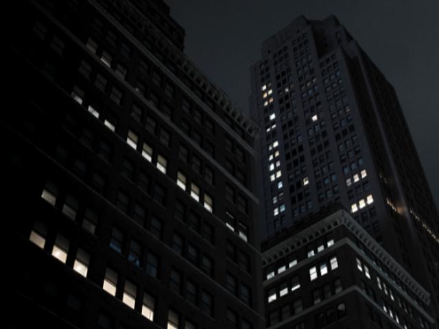 Una escena urbana nocturna con edificios iluminados sutilmente bajo un cielo oscuro.
