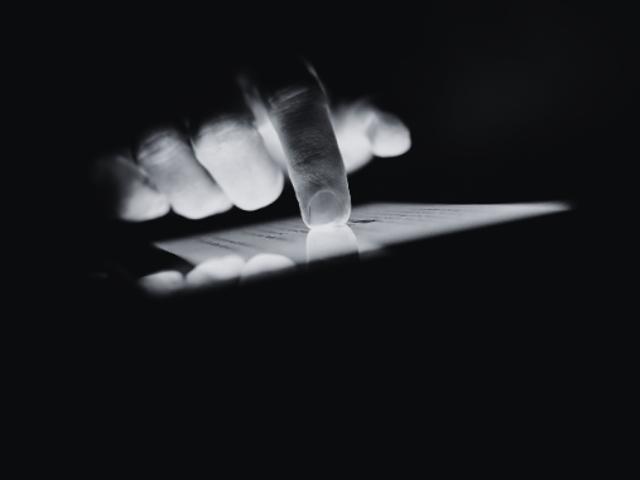 Una mano señala una pantalla iluminada en un entorno oscuro.