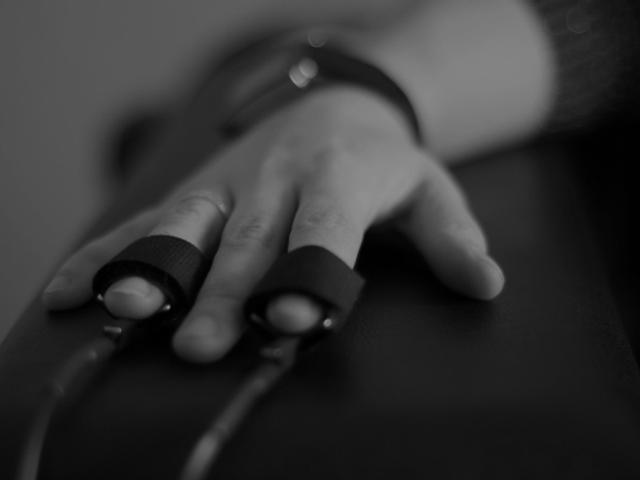 Una mano con anillos en los dedos descansa sobre una superficie oscura.