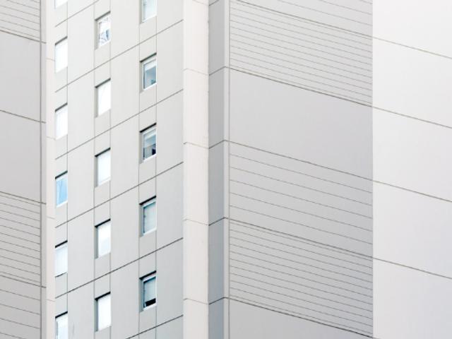 La imagen muestra una fachada de un edificio moderno con líneas horizontales y ventanas.