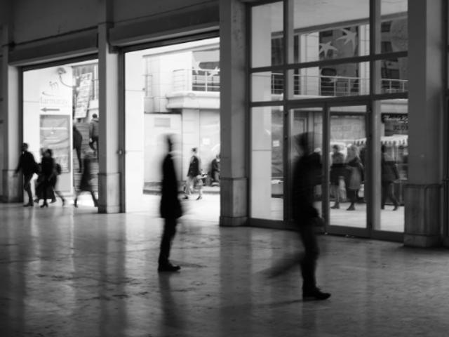 Una imagen en blanco y negro que muestra un espacio interior con personas caminando hacia la salida.