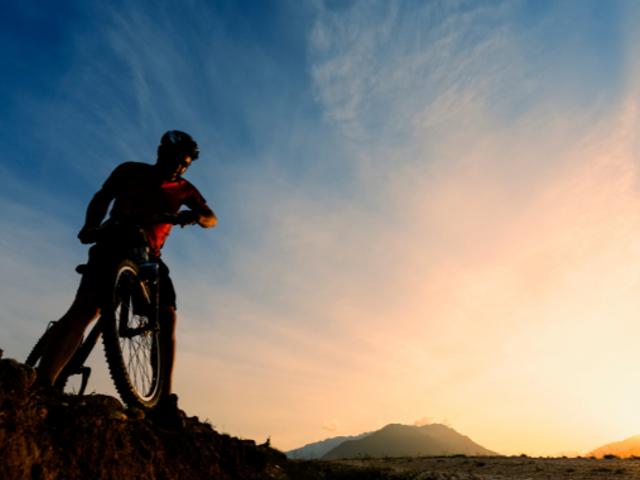 Un ciclista se encuentra en una colina admirando el ocaso.