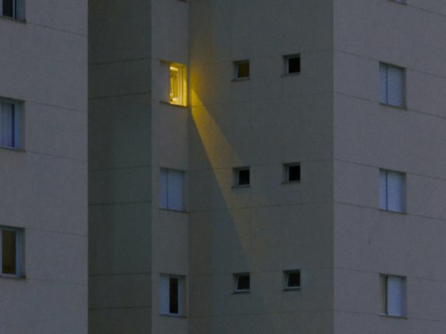 Una luz amarilla se emite desde una ventana de un edificio gris durante la noche.