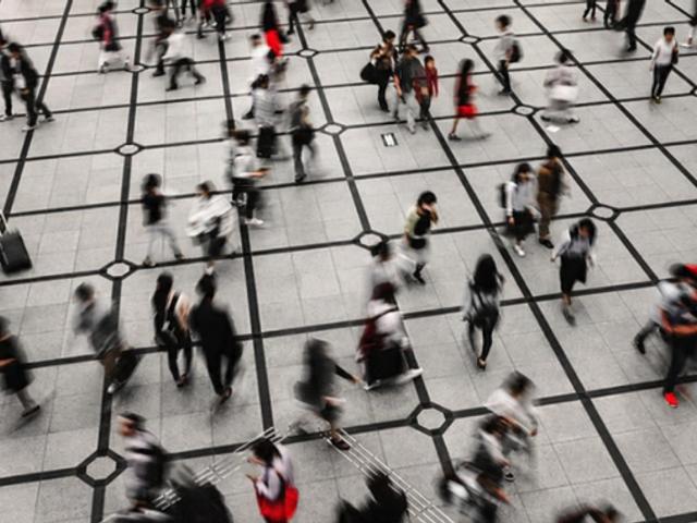 Una multitud de personas se mueve rápidamente por un espacio urbano con un diseño de piso cuadriculado.