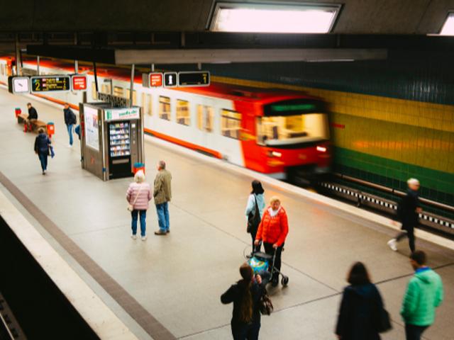 Una estación de tren con pasajeros esperando y un tren en movimiento.