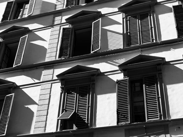 Edificio con ventanas y persianas en contraste de luces y sombras.