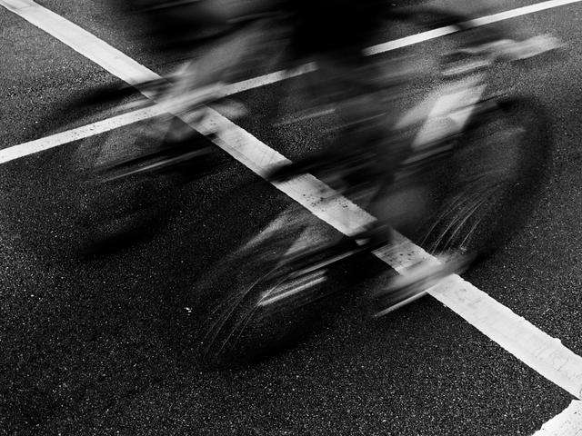 Una imagen en blanco y negro que muestra bicicletas en movimiento cruzando una línea en la carretera.