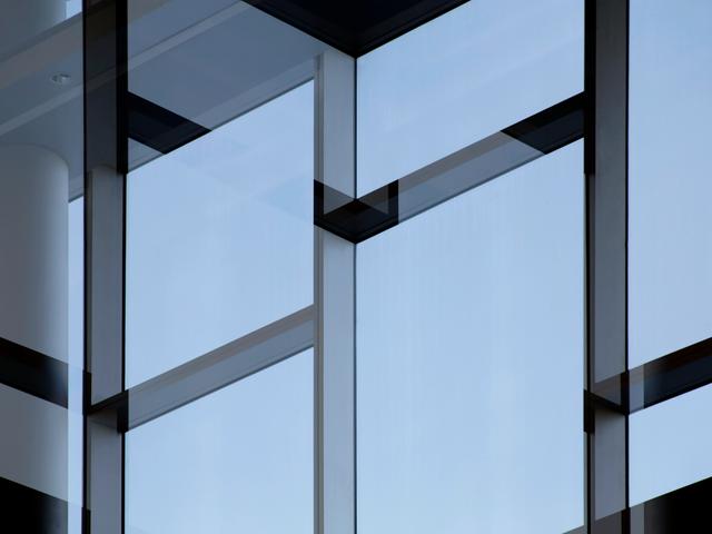 Una fachada moderna de vidrio con patrones geométricos y un cielo azul reflejado.