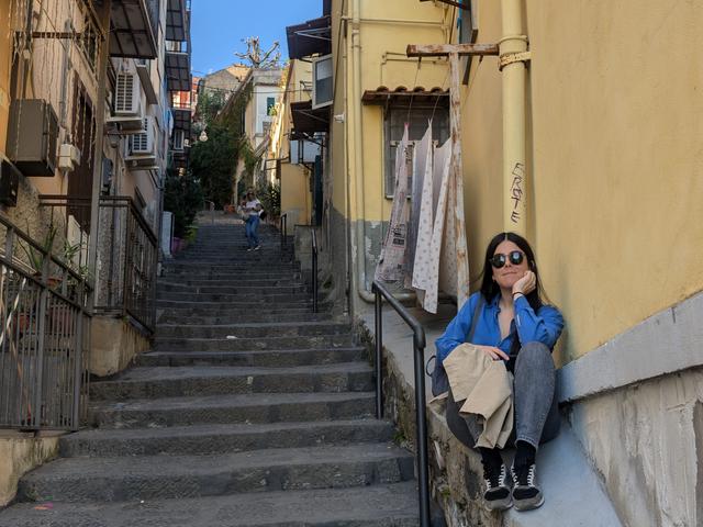 Una persona sentada en las escaleras de una calle estrecha y soleada.