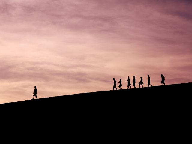 Grupos de personas caminando en una colina durante un atardecer.