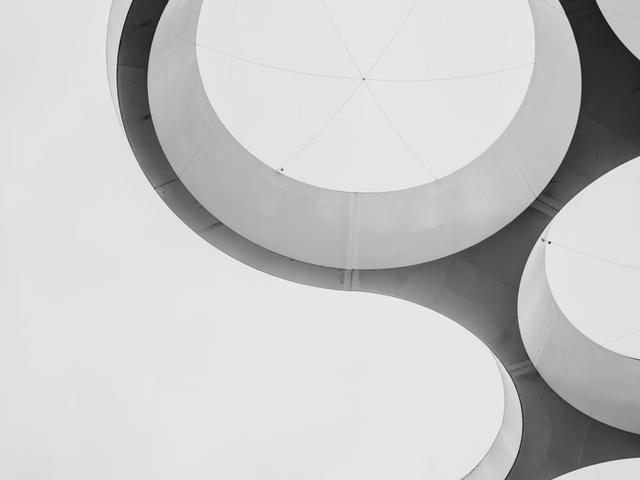 Una estructura arquitectónica moderna con formas circulares y líneas fluidas sobre un fondo nublado.