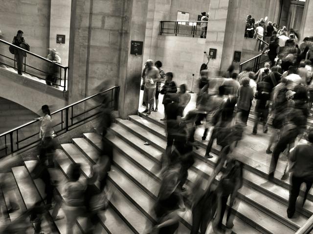 Una multitud de personas se mueve rápidamente por unas escaleras en un espacio arquitectónico moderno.