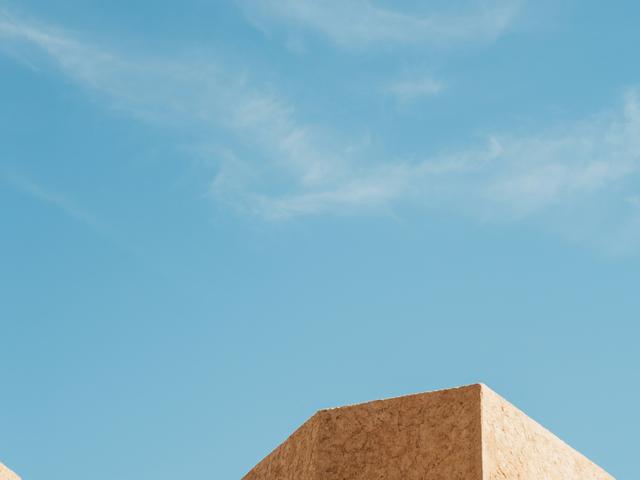 La imagen muestra unas estructuras geométricas en tonos beige contra un cielo azul claro.